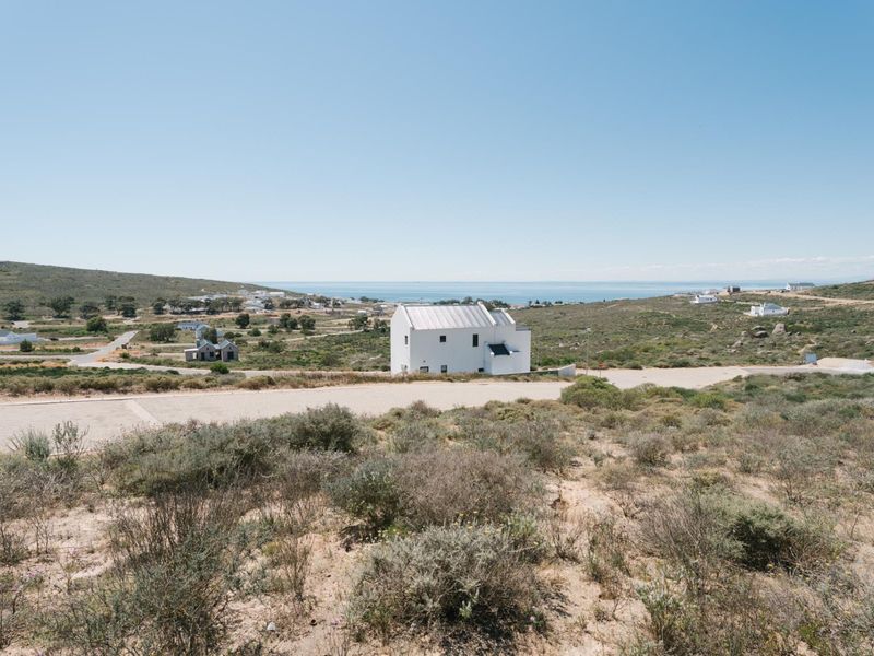 An elevated aerial view of a vacant residential plot featuring natural coastal vegetation, gravel access roads, and distant ocean views.