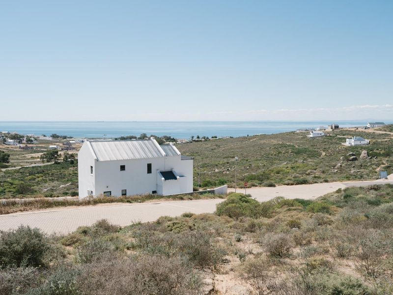 A scenic elevated view of a coastal residential area featuring a white house, paved roads, and expansive ocean views.