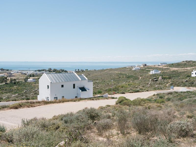 A scenic elevated view of a coastal residential area featuring a modern white house, paved roads, and expansive ocean views.