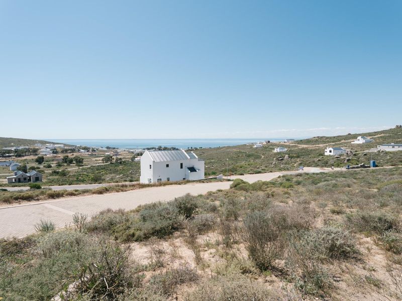 A scenic elevated view of the surrounding coastal landscape, natural vegetation, and local residential development with a paved road in the foreground.