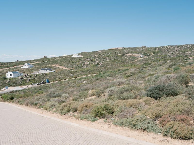 A view of a vacant residential plot featuring natural coastal vegetation and access to a paved road in a developing estate.