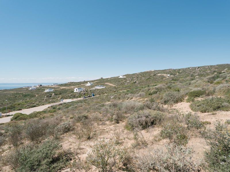 A wide-angle view of the vacant residential land, showcasing the natural coastal landscape, sloped terrain, and surrounding neighbourhood context.