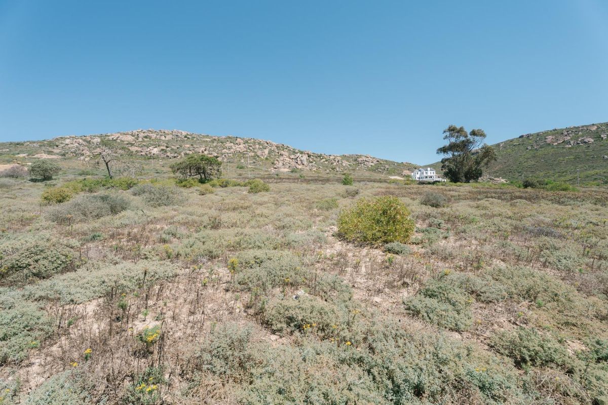 A wide-angle view of the vacant residential land featuring natural rocky terrain and native vegetation under a clear blue sky.