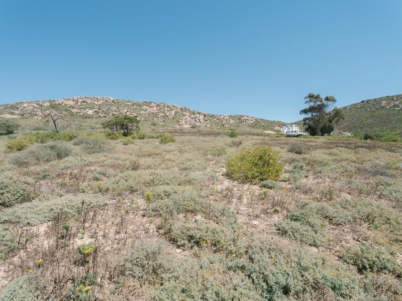 A wide-angle view of the vacant residential land featuring natural rocky terrain and native vegetation under a clear blue sky.