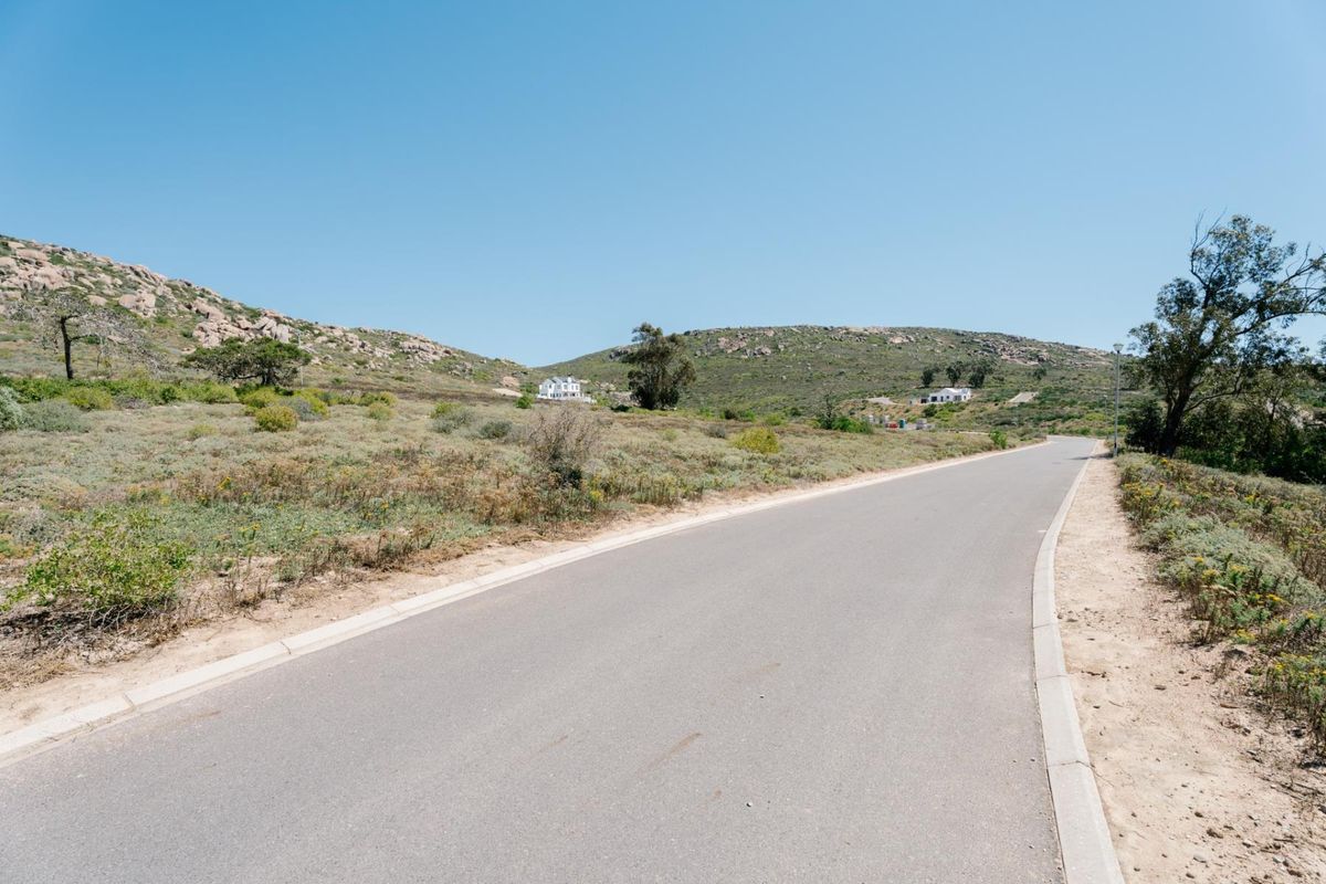A view of a paved residential street winding through a natural, hilly landscape with native vegetation.