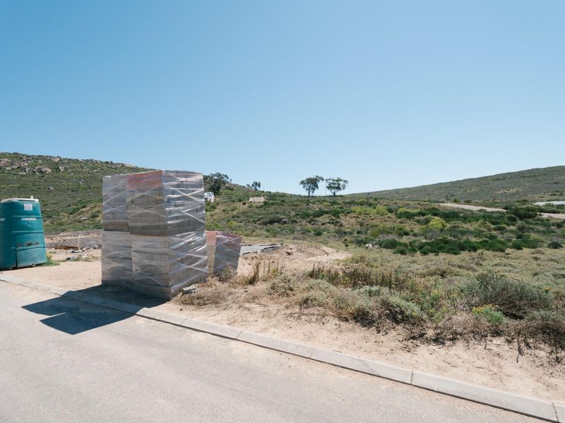 A vacant residential plot featuring a paved road frontage, concrete curbing, and natural hillside landscape, ready for development.