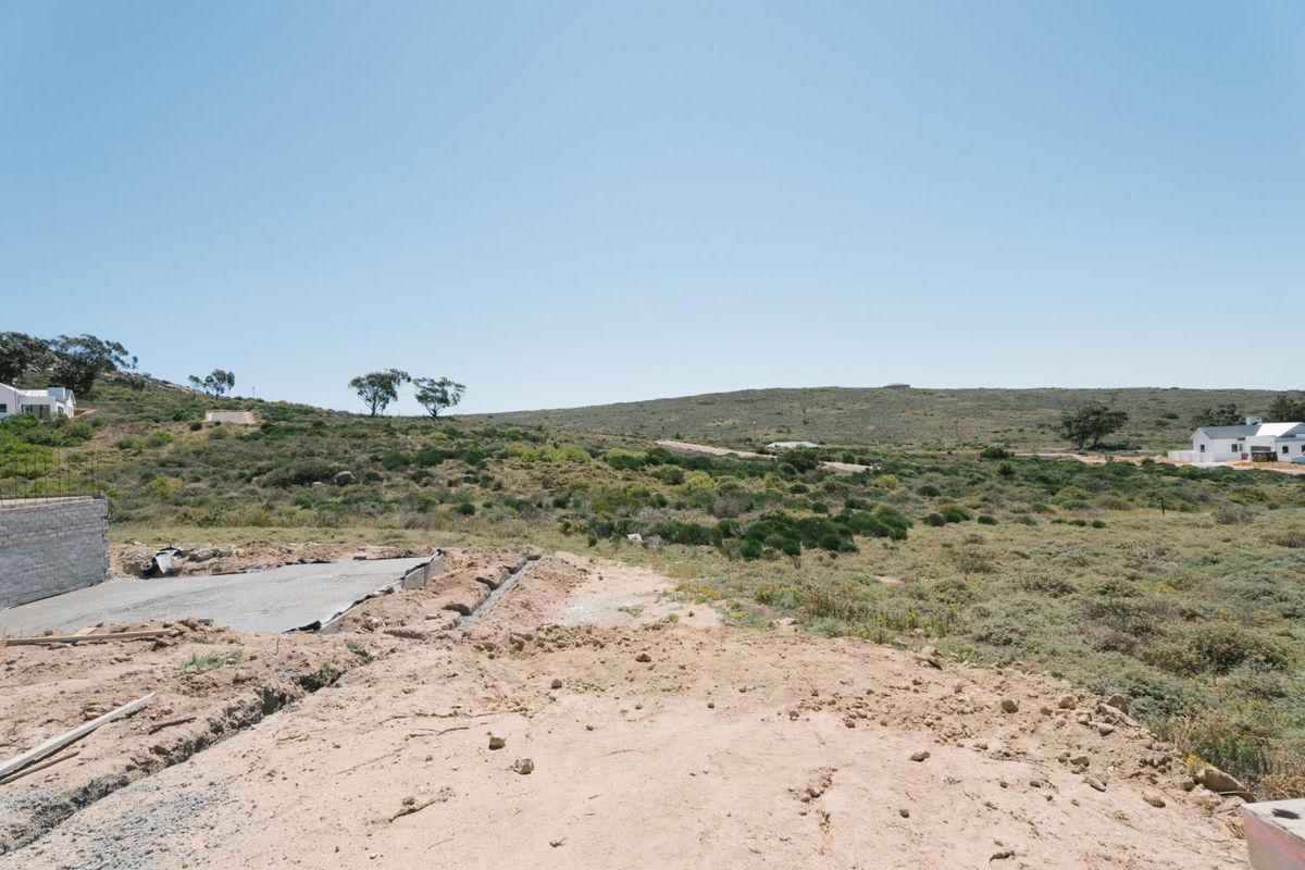 A view of a vacant residential plot showing a concrete foundation and retaining wall under construction with surrounding natural landscape.