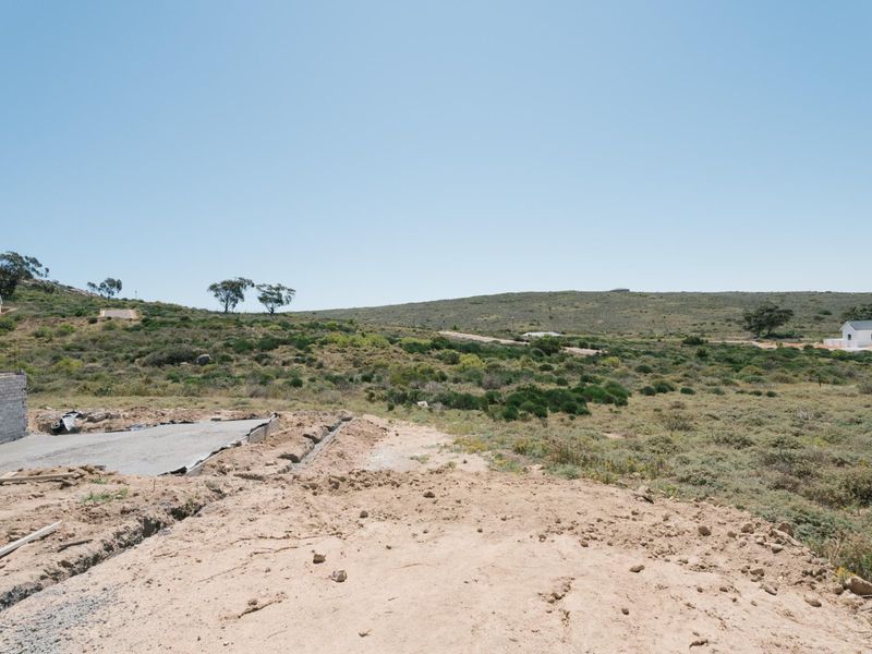 A view of a vacant residential plot showing a concrete foundation and retaining wall under construction with surrounding natural landscape.