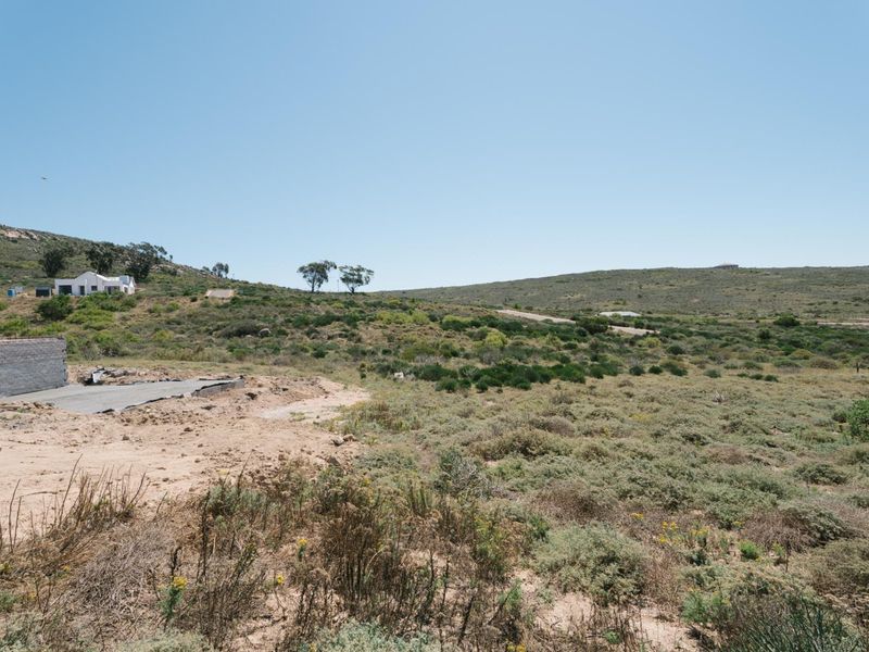 A vacant residential plot featuring a partially constructed concrete foundation and masonry wall, set within a natural landscape.