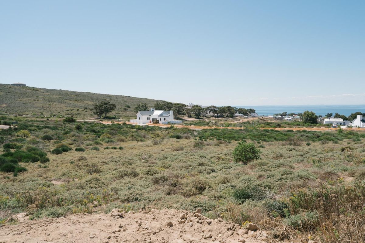 A wide-angle view of a coastal residential area featuring natural fynbos vegetation and distant ocean views.
