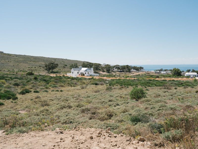 A wide-angle view of a coastal residential area featuring natural fynbos vegetation and distant ocean views.