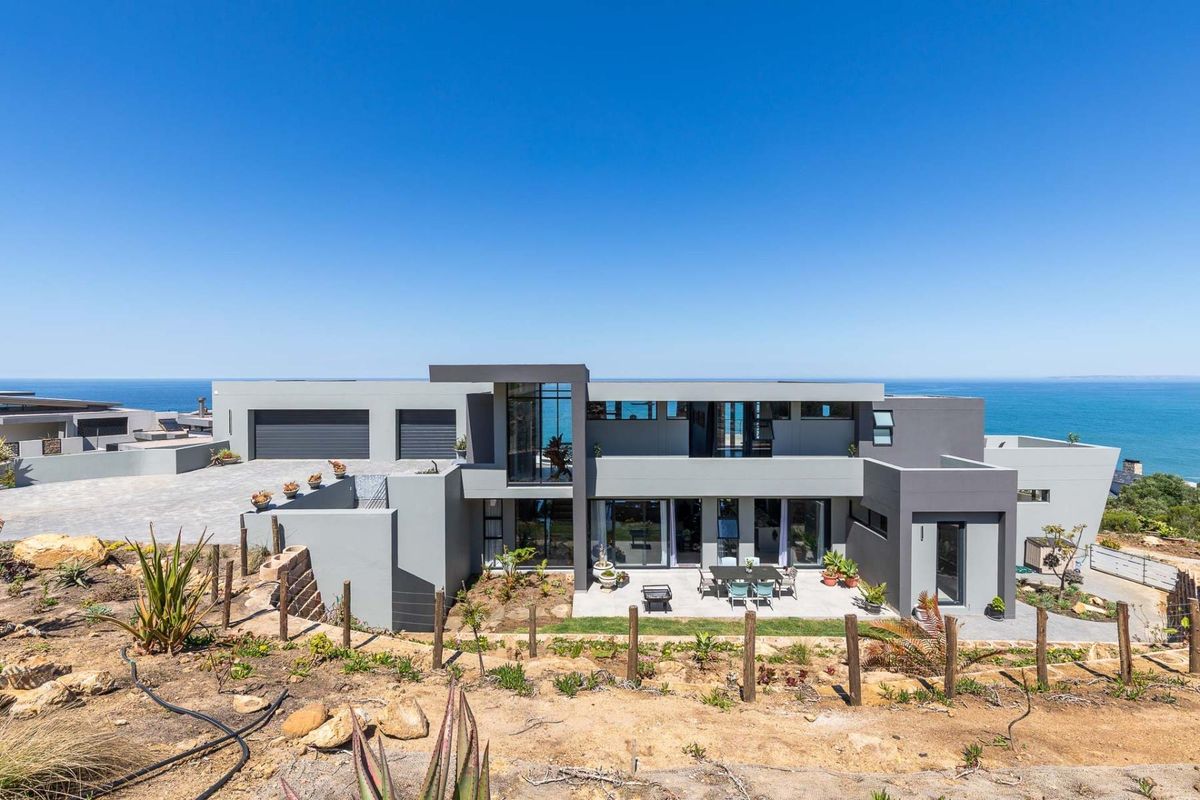 Modern multi-level coastal residence featuring a sleek grey facade, double garage, and expansive patio area overlooking the ocean.