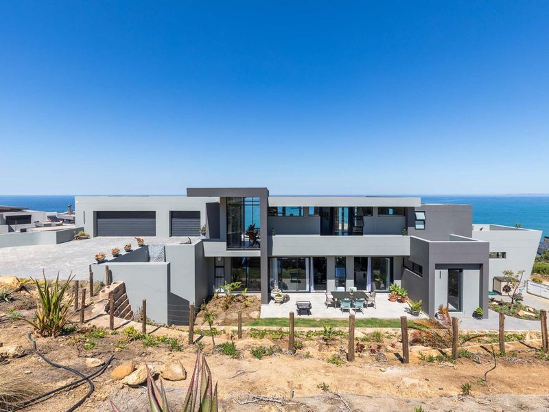 Modern multi-level coastal residence featuring a sleek grey facade, double garage, and expansive patio area overlooking the ocean.