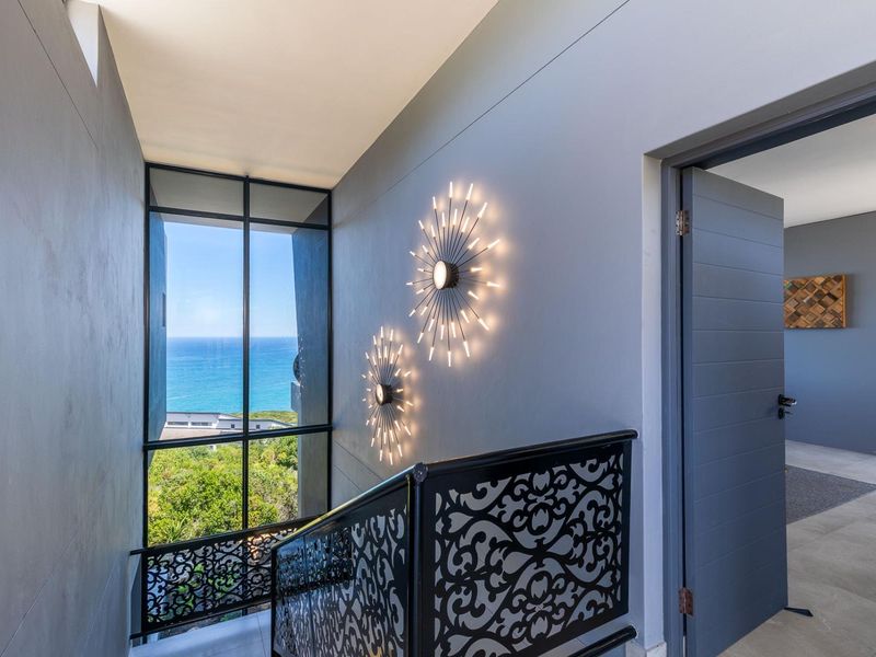 A modern, well-lit hallway featuring a decorative metal balustrade, floor-to-ceiling windows with ocean views, and contemporary wall lighting.