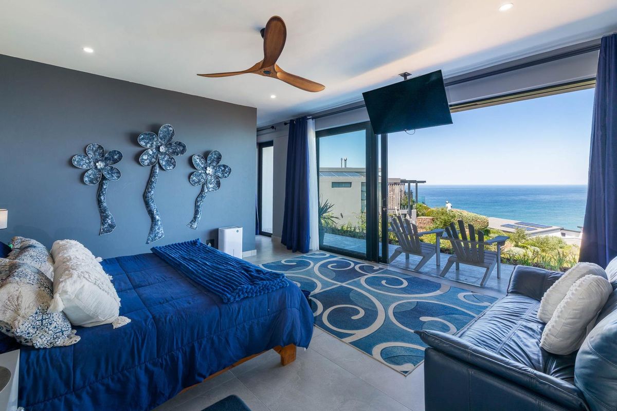 Spacious bedroom featuring modern tiled flooring, recessed lighting, a ceiling fan, and large sliding glass doors opening to a scenic ocean view.