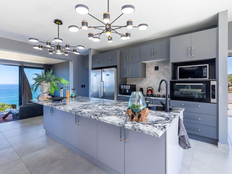 Modern open-plan kitchen featuring a large marble island, high-end built-in appliances, and contemporary lighting, seamlessly flowing into a living area with ocean views.