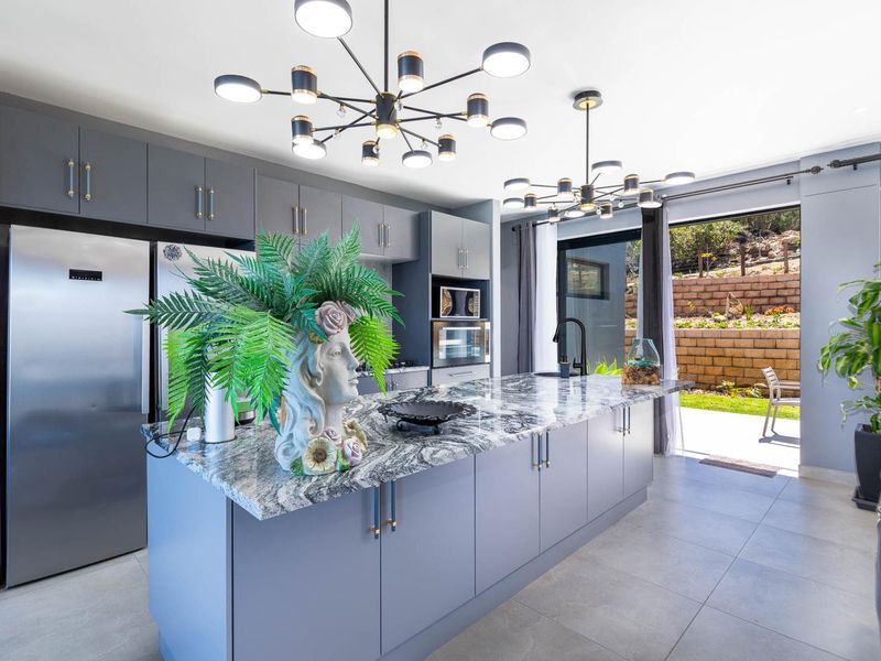 Modern kitchen featuring a large island with granite countertops, sleek grey cabinetry, built-in appliances, and contemporary pendant lighting, with direct access to the rear patio.