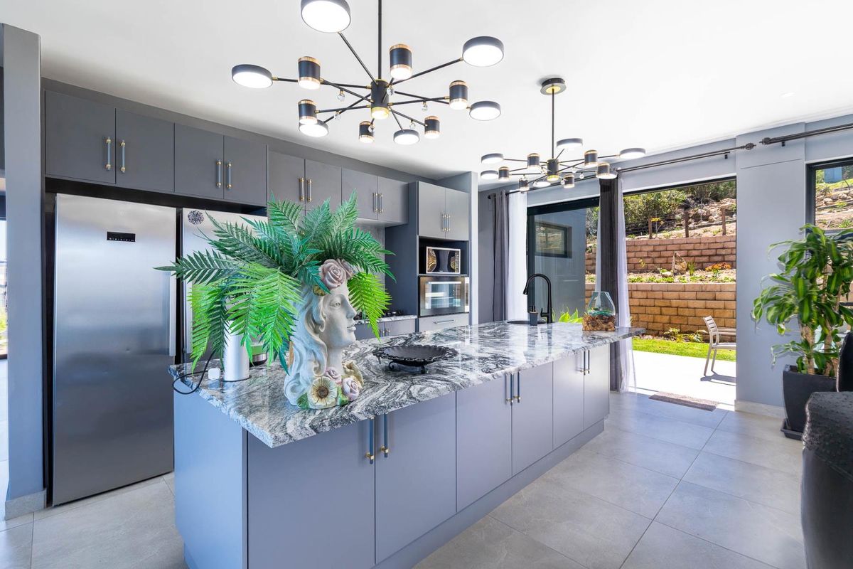 Modern kitchen featuring a large island with granite countertops, sleek grey cabinetry, built-in appliances, and contemporary pendant lighting, with direct access to the rear patio.