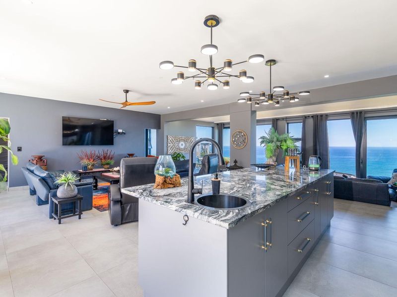 Spacious open-plan living area featuring a modern kitchen island with stone countertops, contemporary pendant lighting, and expansive ocean views.