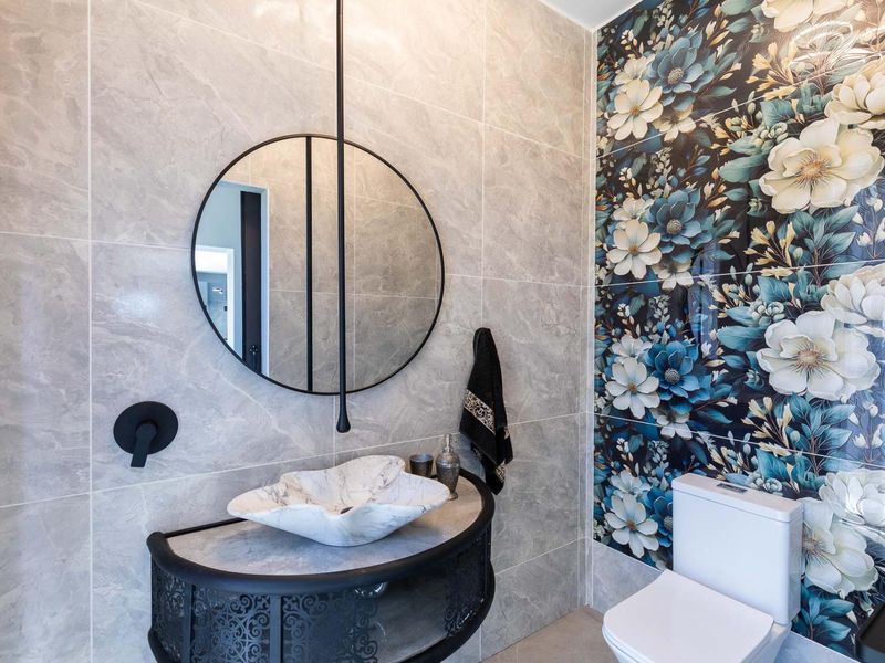 Modern bathroom featuring a unique stone vessel sink, wall-mounted faucet, decorative floral feature wall, and contemporary vanity cabinet.
