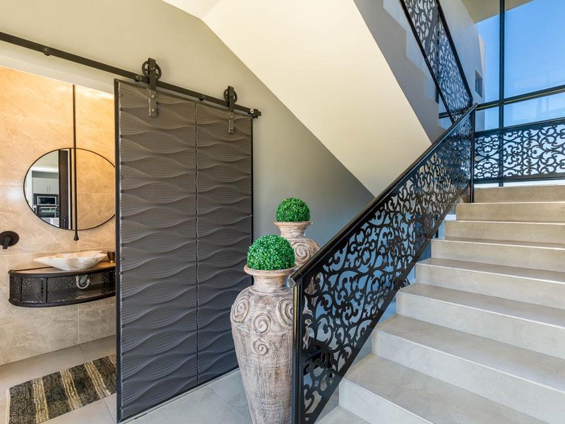 Elegant entrance area featuring a modern staircase with intricate wrought iron balustrade, stone wall accents, and a stylish sliding barn door leading to a guest bathroom.