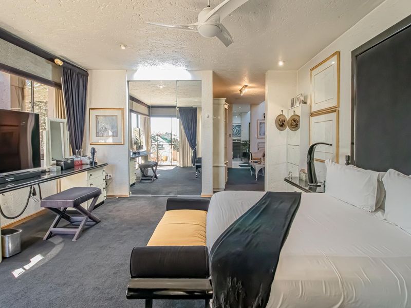 Spacious bedroom featuring a built-in vanity, mirrored wardrobe doors, and a ceiling fan, with direct access to an adjoining living area.