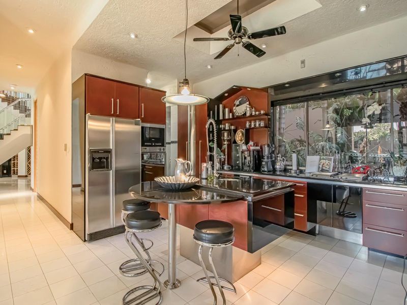 Modern kitchen featuring dark wood cabinetry, a central island with breakfast bar, integrated appliances, and tiled flooring, with an open view to the staircase.