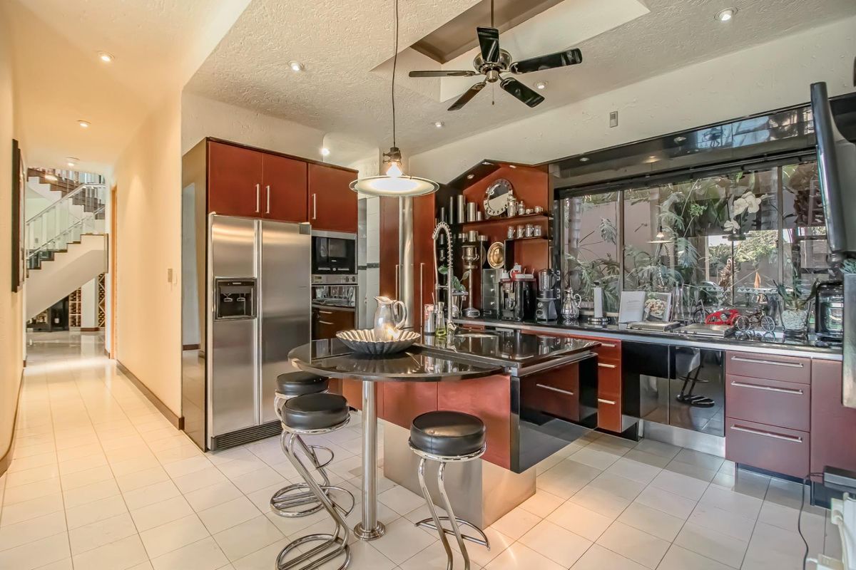 Modern kitchen featuring dark wood cabinetry, a central island with breakfast bar, integrated appliances, and tiled flooring, with an open view to the staircase.