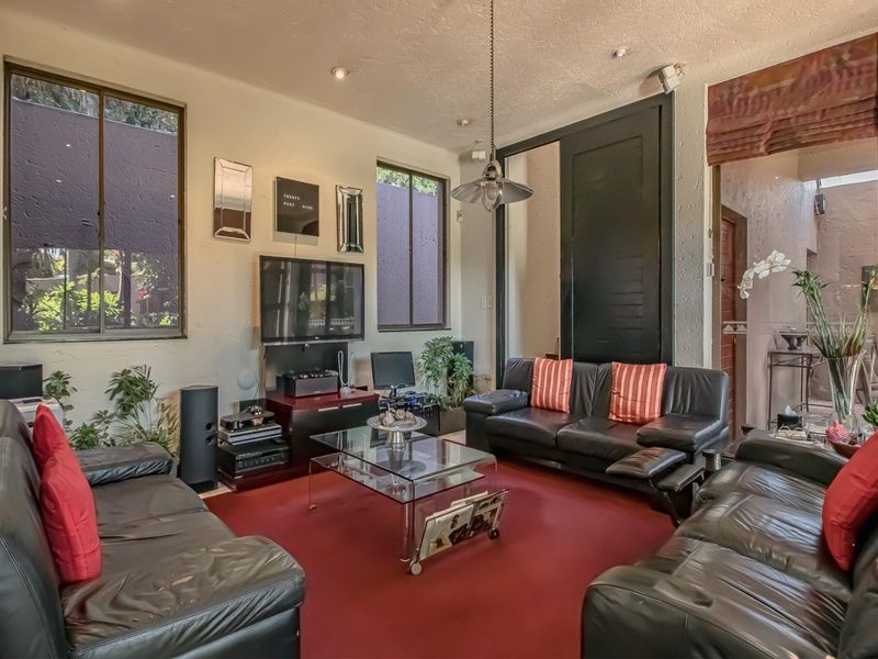 A comfortable living room featuring recessed downlights, a central pendant light, and large aluminium-framed windows that provide natural light.