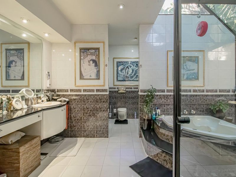Spacious bathroom featuring a built-in vanity, integrated sink, large bathtub, and separate toilet area with tiled finishes and recessed lighting.
