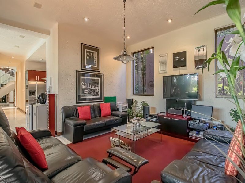 A spacious living room featuring recessed lighting, a pendant light fixture, and tiled flooring, with an open-plan layout leading to the kitchen area.