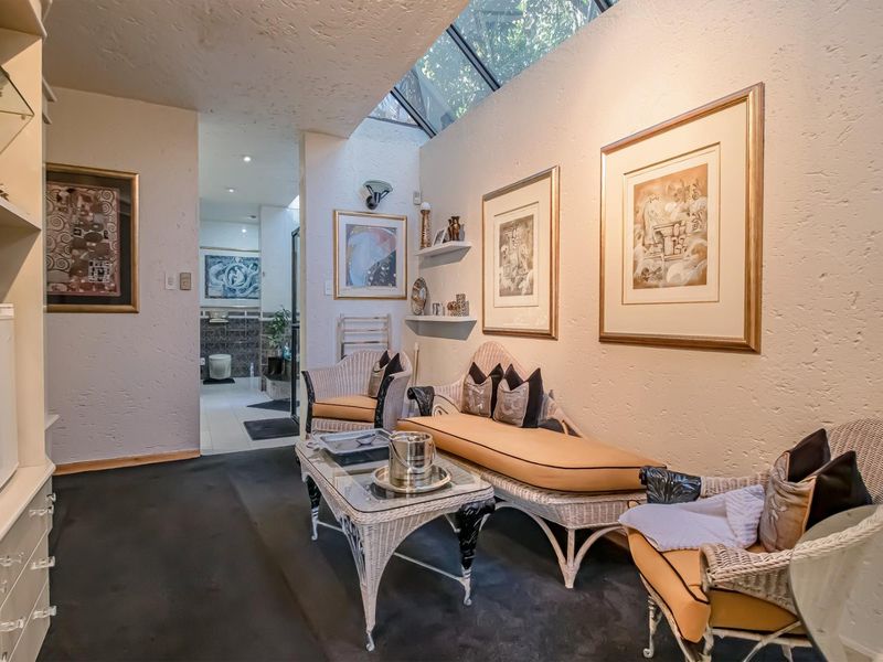 A cozy living area featuring a large skylight that provides natural light, textured wall finishes, and built-in shelving, leading into an adjacent bathroom space.