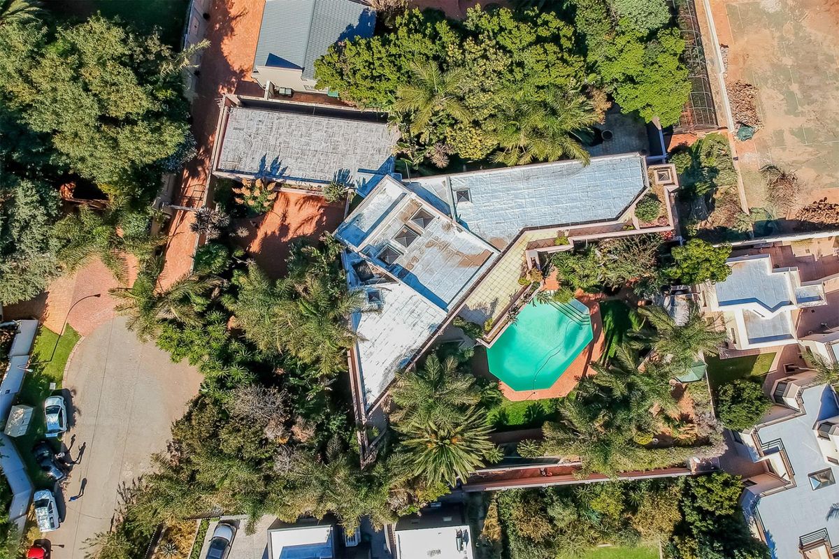 Aerial view of the property showcasing the unique roof structure, swimming pool, mature garden, and paved driveway access.