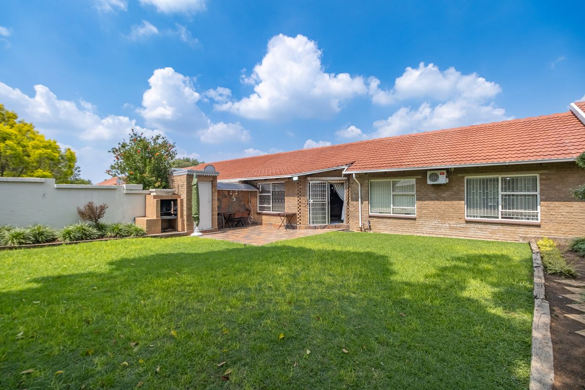 Rear view of the townhouse featuring a well-maintained lawn, paved patio area with a built-in braai, and brick exterior finish.