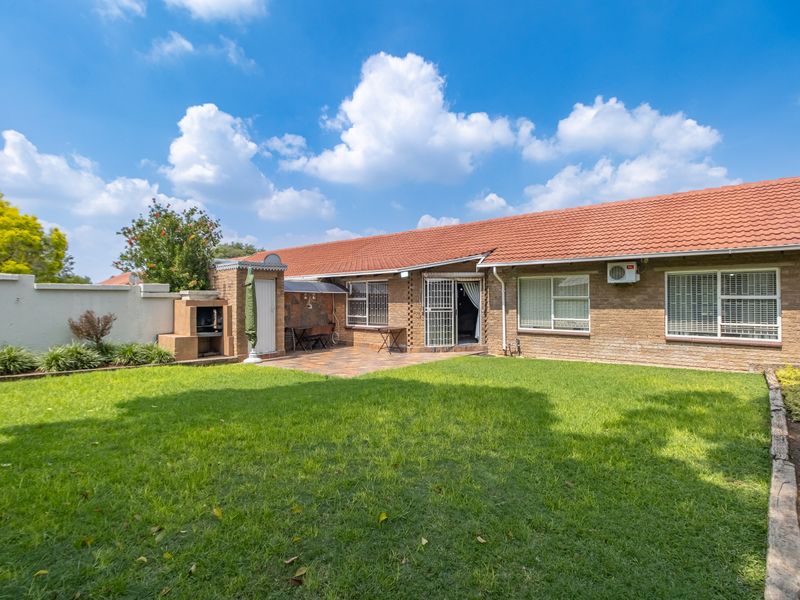 Rear view of the townhouse featuring a well-maintained lawn, paved patio area with a built-in braai, and brick exterior finish.