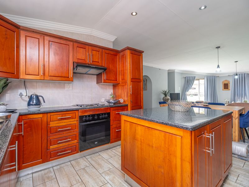 Open-plan kitchen featuring warm wooden cabinetry, granite countertops, a central island, and integrated appliances, flowing seamlessly into the adjacent living and dining area.