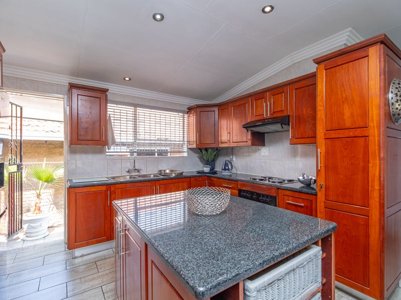 A well-maintained kitchen featuring warm wooden cabinetry, granite countertops, a central island, and direct access to an outdoor patio area.