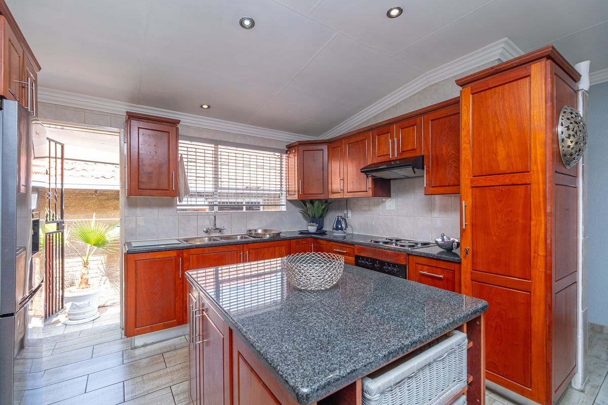 A well-maintained kitchen featuring warm wooden cabinetry, granite countertops, a central island, and direct access to an outdoor patio area.