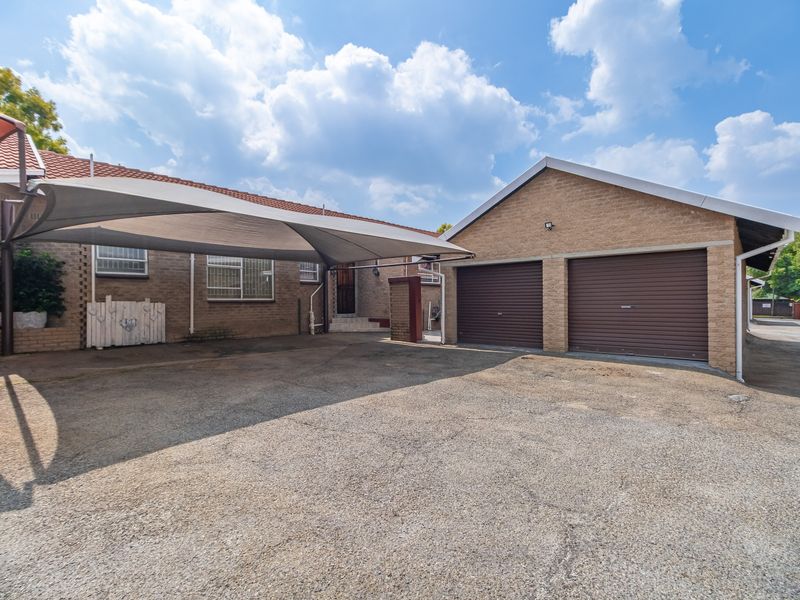Front exterior view of the townhouse featuring a double garage, paved driveway, and a shade sail carport structure.