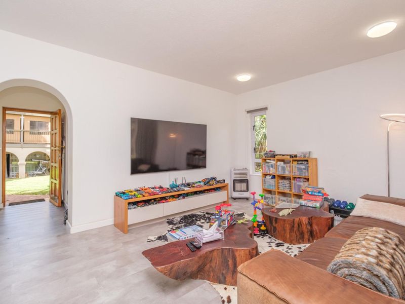 A bright living room featuring an arched entryway, modern laminate flooring, and recessed lighting, with direct access to an outdoor area.