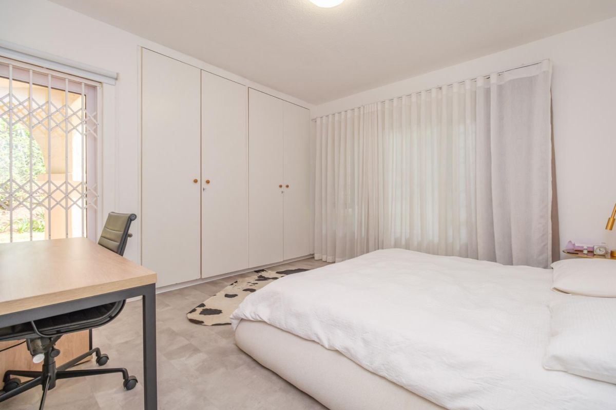 A bright bedroom featuring built-in cupboards, neutral flooring, and a sliding door with a security gate leading to the exterior.
