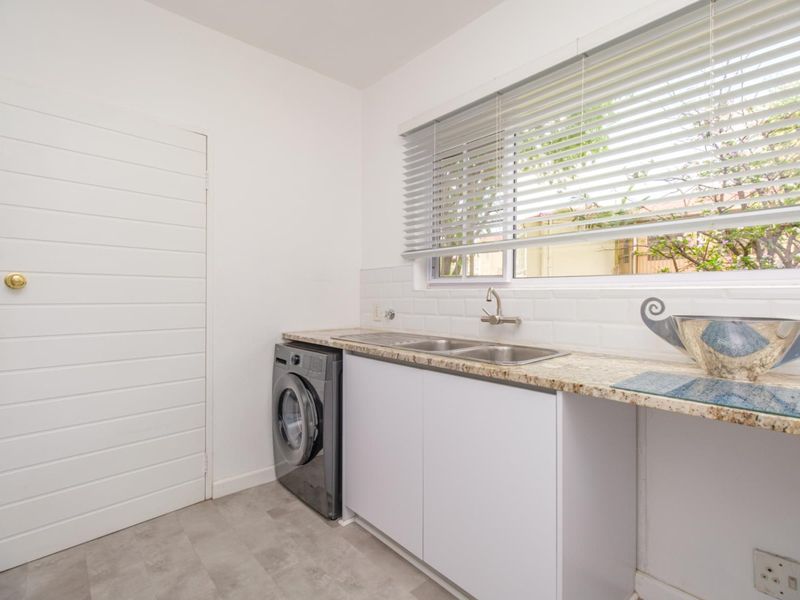 A clean and functional laundry room featuring a stainless steel sink, granite countertops, subway tile backsplash, and built-in cabinetry.