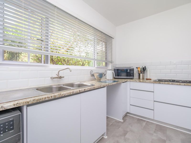 A clean, modern kitchen featuring white cabinetry, granite countertops, a double stainless steel sink, and a classic subway tile backsplash.
