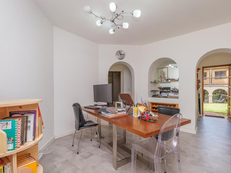 A bright living area featuring arched architectural openings, a built-in wall niche, and modern laminate flooring, providing a versatile space with direct outdoor access.