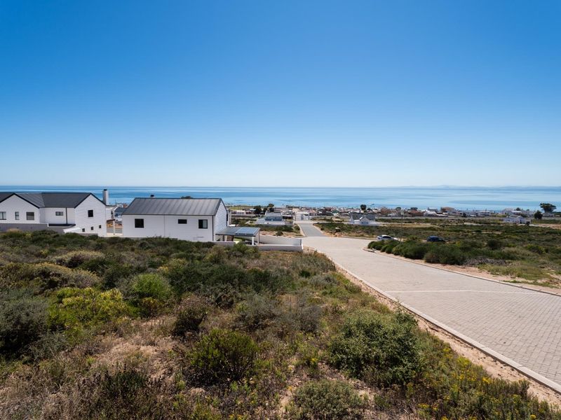 An elevated aerial view of a residential development featuring paved roads and coastal scenery with ocean views.