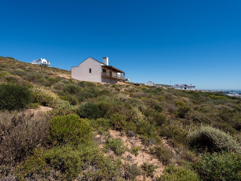 A view of the rear elevation of a residential property situated on a sloped, natural landscape with an elevated deck and chimney.
