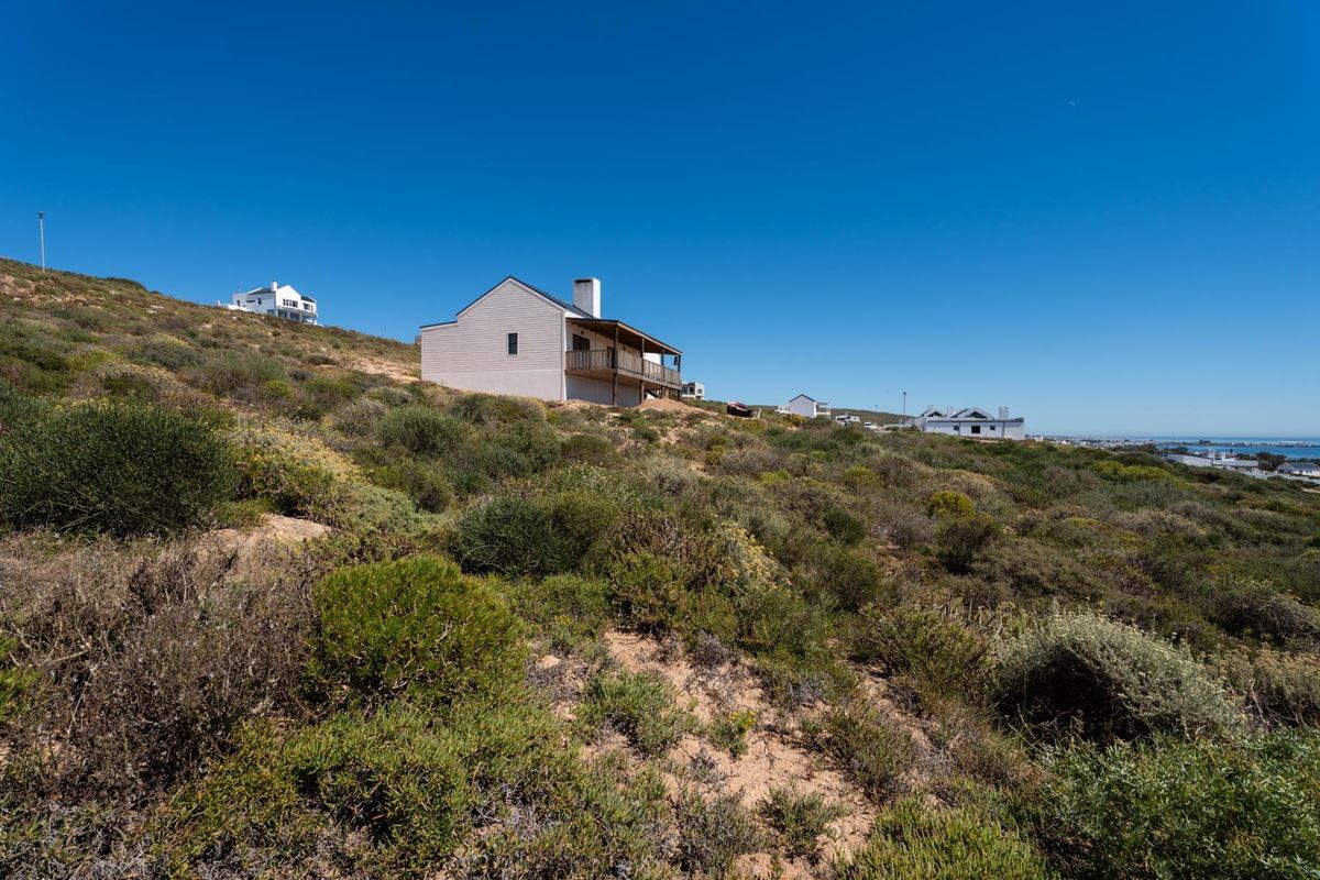 A view of the rear elevation of a residential property situated on a sloped, natural landscape with an elevated deck and chimney.