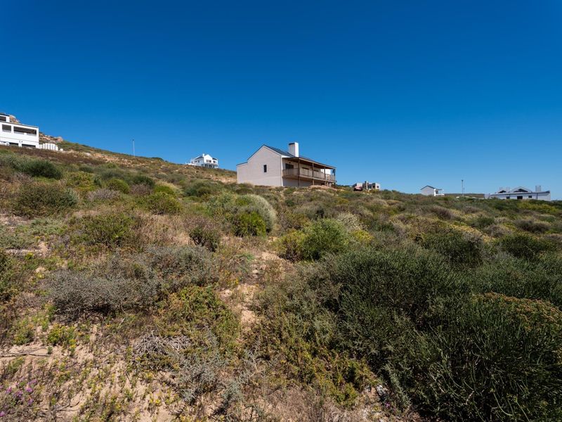 A view of a residential property situated on a sloped, natural coastal landscape with native vegetation.