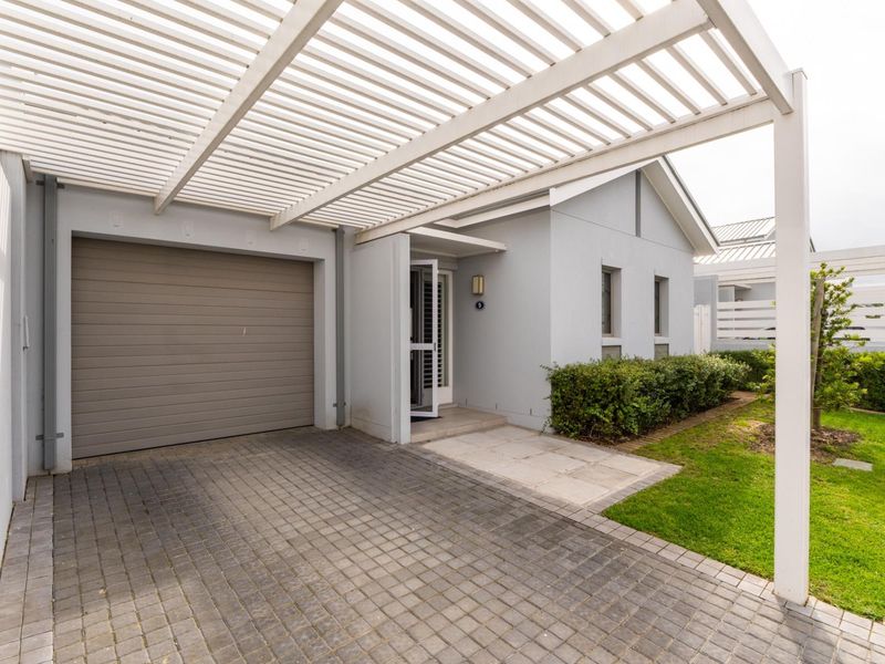 Front exterior view featuring a paved driveway, a covered pergola, a single garage, and a neat landscaped garden.