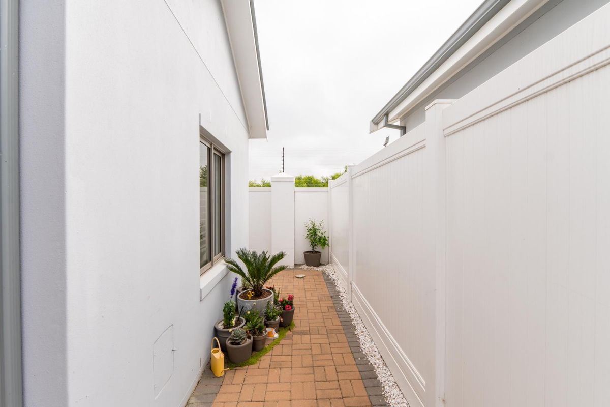 A clean side passage featuring paved brick walkway, white vinyl privacy fencing, and integrated electric security fencing.